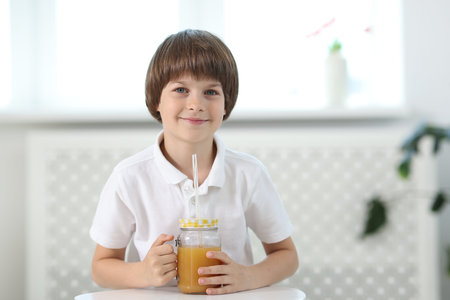 Little boy with mason jar of orange juice at table indoors. Refreshing drinkの写真素材