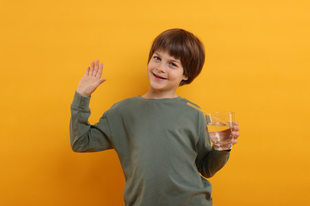 Cute little boy with glass of refreshing soda drink on orange backgroundの写真素材