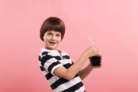 Cute little boy with glass of refreshing soda drink on pink backgroundの写真素材