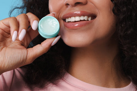 Smiling woman with lip balm on light blue backgroundの写真素材