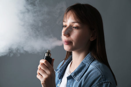 Woman using electronic smoking device on grey background