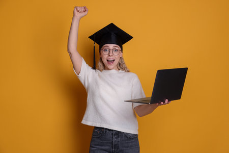 Happy student with laptop after graduation on orange backgroundの写真素材