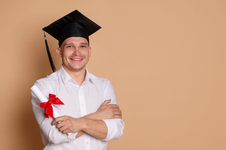 Happy student with diploma after graduation on beige background. Space for textの写真素材
