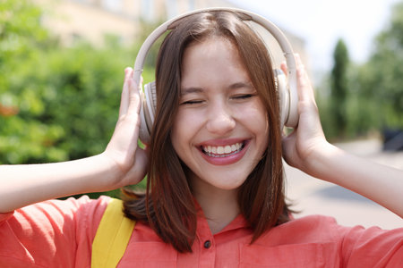 Smiling teenage girl in headphones listening to music outdoors, closeup