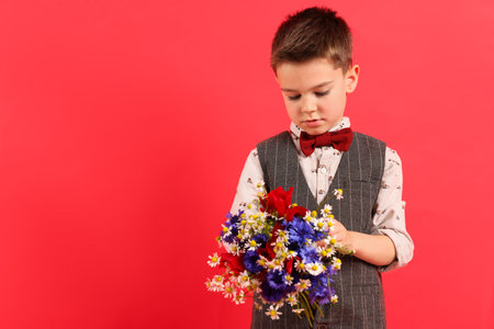 Cute little boy with bouquet of beautiful flowers on red background. Space for textの写真素材