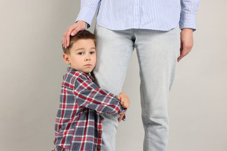 Little boy afraid to leave without mother and hugging her on grey background. Separation anxiety