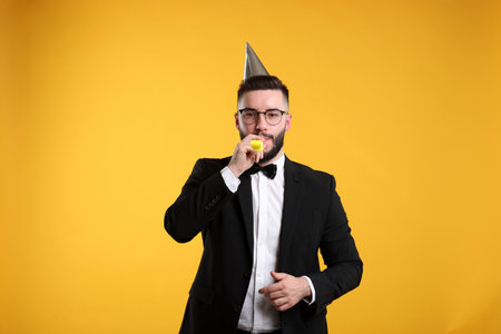 Happy Birthday. Handsome man with party hat and blower on orange backgroundの写真素材