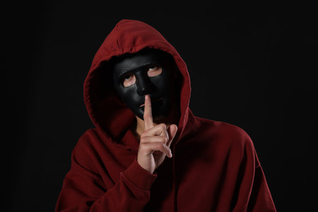 Anonymity. Man with mask showing hush gesture on dark backgroundの写真素材