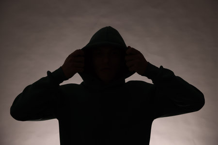 Silhouette of anonymous man in hood on grey backgroundの写真素材