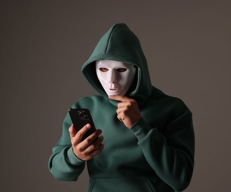 Anonymity. Masked man with smartphone on grey backgroundの写真素材