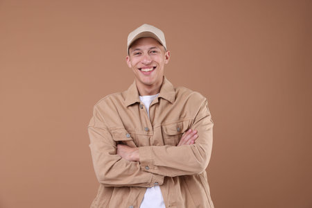 Young man wearing stylish beige baseball hat on light brown background