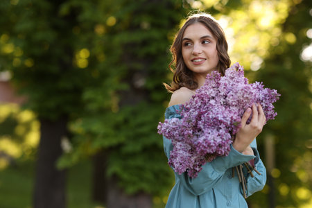 Smiling woman with bouquet of lilac flowers outdoors in morning. Space for textの写真素材