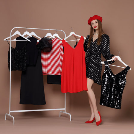 Smiling fashion stylist choosing dress and clothing rack on beige backgroundの写真素材