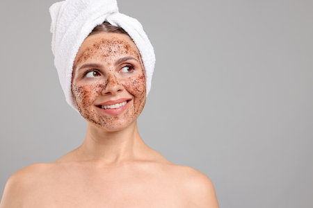Smiling woman with body scrub on her face against grey background. Space for textの写真素材