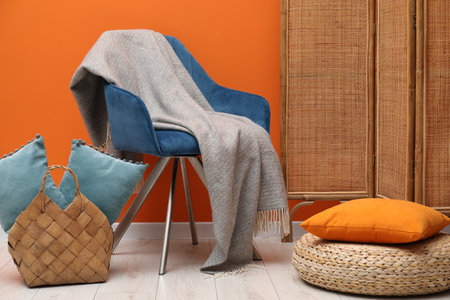 Comfortable armchair with woolen blanket and pillows near orange wall indoorsの写真素材