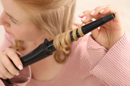 Woman curling her beautiful hair indoors, closeupの写真素材