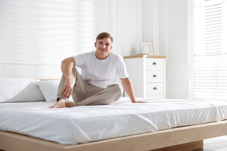 Young man lying on bed with soft mattress at homeの写真素材