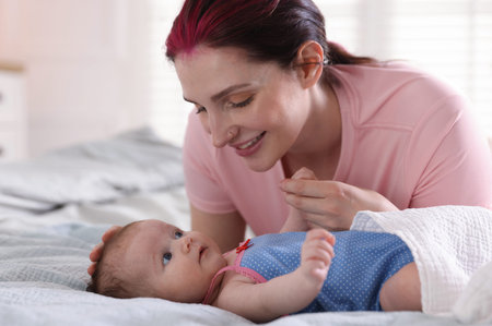 Mother putting her cute newborn baby to sleep on bed at home