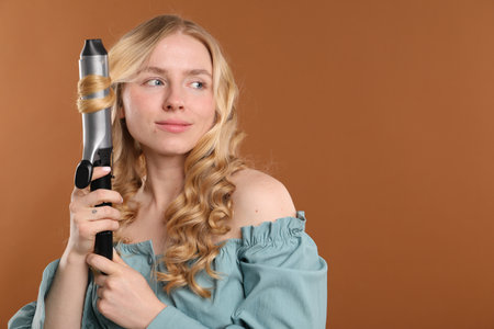 Woman curling her hair on brown background. Space for textの写真素材