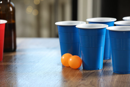 Beer pong game. Plastic cups with drinks and balls on wooden table, closeup. Space for textの写真素材
