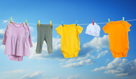 Different baby clothes drying on washing line against blue skyの写真素材