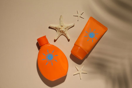 Sunscreen products and sea stars on beige background, top view. Bottle and tube with drawings of sun