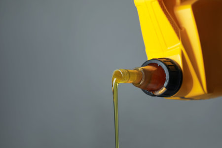Pouring motor oil from yellow canister on gray background, closeup. Space for textの写真素材