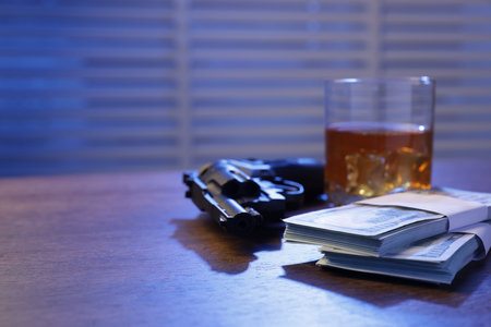 Mafia and criminal world. Gun, whiskey and money on wooden table indoors, closeup. Space for textの写真素材