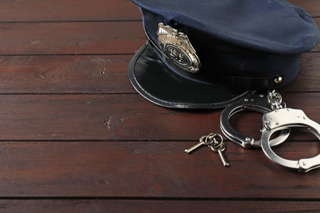 Police cap, handcuffs and keys on wooden table, closeup. Space for textの写真素材