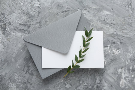 Blank invitation card, branch and envelope on gray textured table, top viewの写真素材