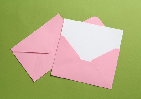 Blank invitation card and envelopes on green background, flat lay. Space for designの写真素材