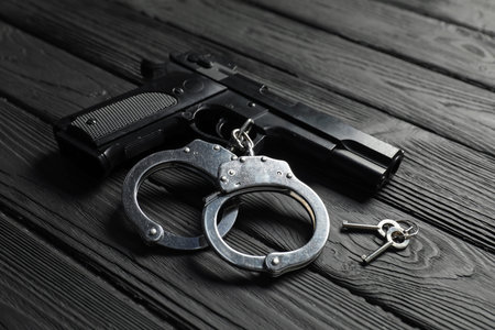 Gun, handcuffs and keys on black wooden table, closeup. Police equipmentの写真素材