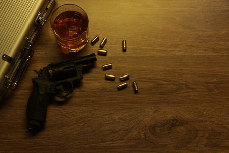 Mafia and criminal world. Gun, bullets, whiskey and briefcase on wooden table, flat lay. Space for textの写真素材