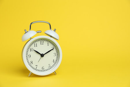 One white alarm clock on yellow background, space for textの写真素材