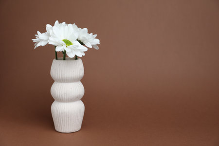 Beautiful white flowers in vase on brown background, space for textの写真素材