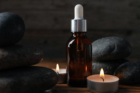 Spa composition with stones, dropper and burning candles on wooden table against black background, closeupの写真素材