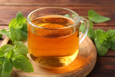 Aromatic lemon balm tea in glass cup and fresh leaves on table, closeup