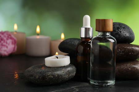 Spa composition with wet stones, cosmetic products and burning candles on dark textured table against blurred green background, selective focusの写真素材