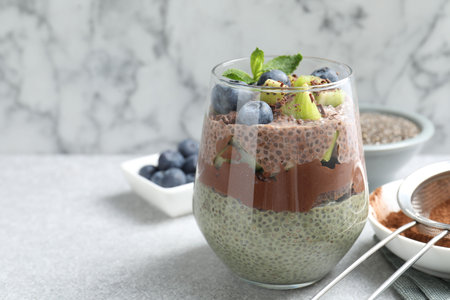 Delicious chocolate pudding with chia seeds, kiwi, mint and blueberries in glass on gray textured table against marble background, closeup. Space for textの写真素材