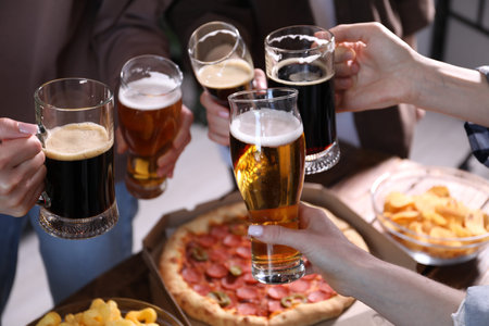 Friends clinking glasses of beer at table, closeup