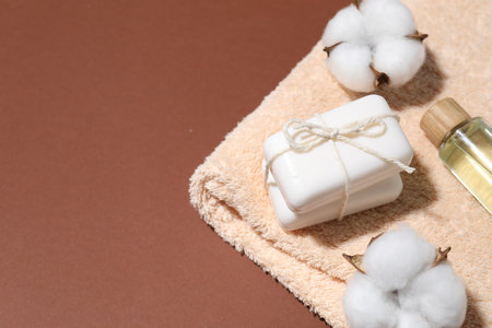 Soap bars, cosmetic product, towel and cotton flowers on brown background, above view. Space for textの写真素材