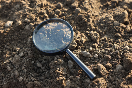Magnifying glass on dry soil in field, closeup