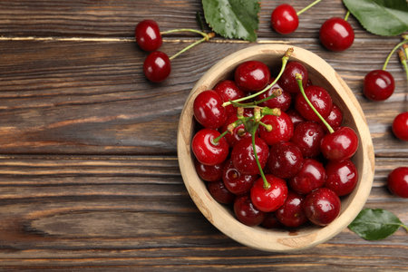 Fresh wet cherries in bowl and leaves on wooden table, flat lay. Space for textの写真素材