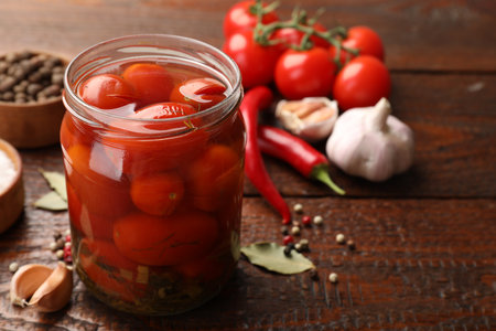 Tasty pickled tomatoes in jar and ingredients on wooden table, closeupの写真素材
