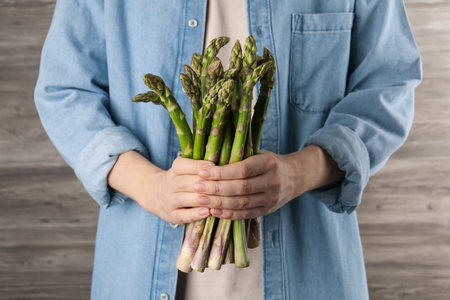 Woman holding fresh raw asparagus near wooden wall, closeupの写真素材