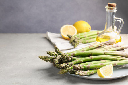 Fresh raw asparagus, oil and lemon on light gray table, closeup. Space for textの写真素材