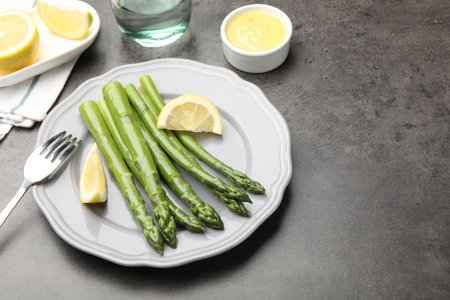 Tasty cooked asparagus served with lemon on gray table, space for textの写真素材