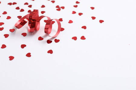 Shiny red party streamer and heart shaped confetti on white background, closeup. Space for textの写真素材