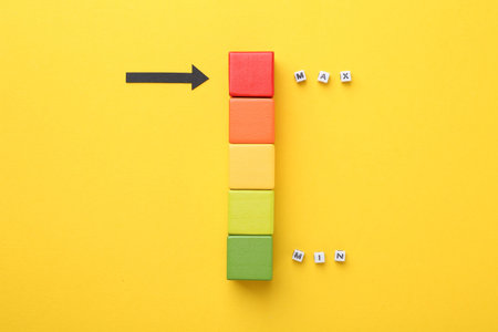 Words Min and Max, colorful cubes and arrow pointing at red one on yellow background, flat lay