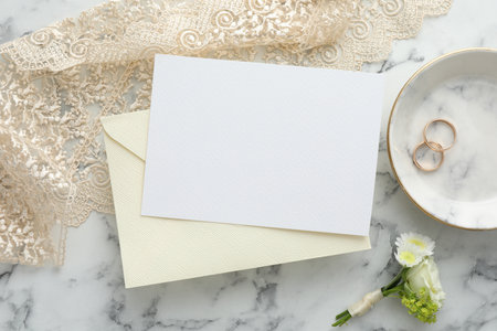 Wedding invitation card, envelope, golden rings and floral decor on white marble table, closeupの写真素材
